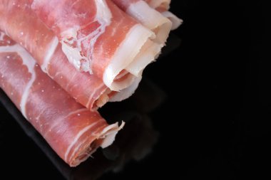 Kavrulmuş domuz jamonu ince katmanlara bölünmüş ve tüplere sarılmış siyah arka plan yakın plan makro fotoğrafçılığında yatıyor.