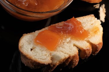 Şeftali reçelli bir dilim beyaz çörek siyah bir arka planda yatıyor.