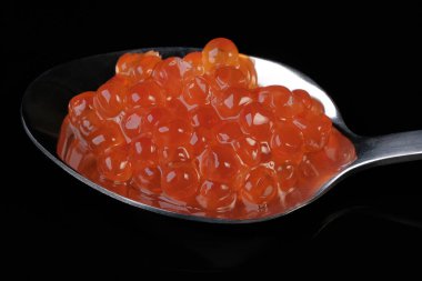 Kırmızı somon balığı havyarı siyah arka planda metal bir kaşıkta uzanıyor. Yakın plan makro fotoğraf çekimi.