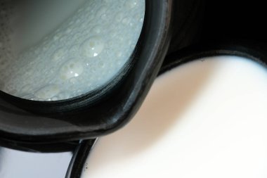 Siyah arka planda siyah bir kase içinde taze pastörize edilmiş inek sütü. Yakın plan makro fotoğraf.