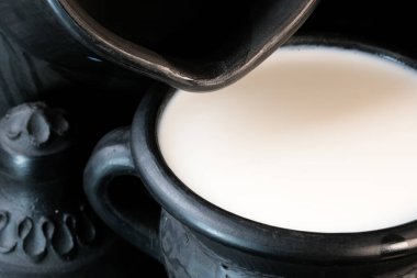 Siyah arka planda siyah bir kase içinde taze pastörize edilmiş inek sütü. Yakın plan makro fotoğraf.