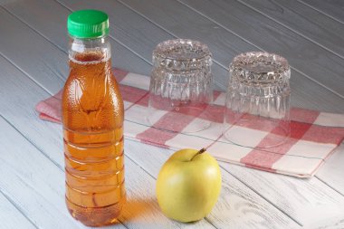 Elma suyu plastik bir şişenin içinde beyaz ahşap arka planda bir elmanın yanında yakın plan makro fotoğrafçılık.