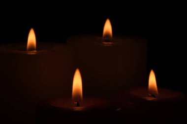 Yas dolu dört parafin kalın mum yakın plan siyah bir fonda yanar.