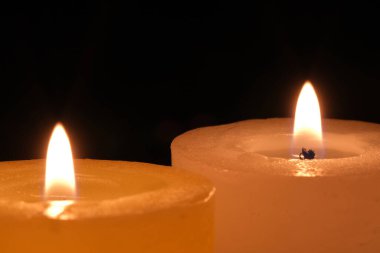 Siyah bir arkaplanda iki parafin kalın mum yanıyor.