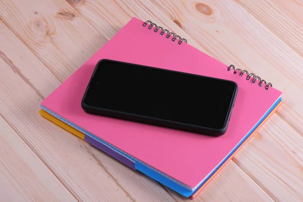 Black smartphone on notepad with pink cover layout composition with loose-leaf notebook