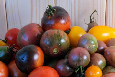Çok renkli, olgun, farklı türde küçük domatesler, ahşap bir masa üzerinde, yakın çekim makro fotoğrafçılığında yatıyor.