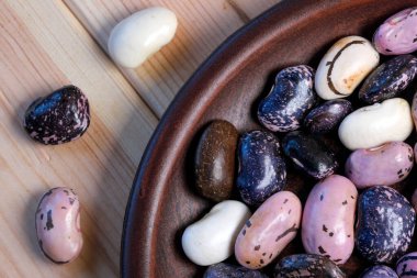 Kahverengi ahşap arka planda, kilden bir tabakta çok renkli taze fasulyeler.