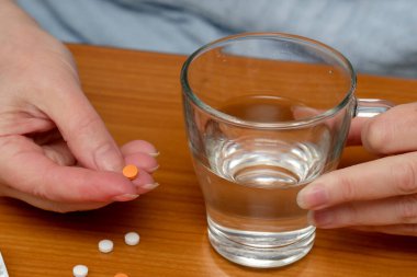 Bir insan küçük bir portakal hapı ve bir bardak su tutar..