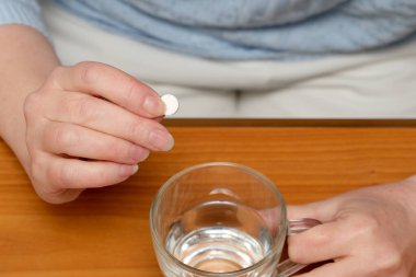 İnsan evinde su içmeye hazırlanırken elinde bir hap tutar..