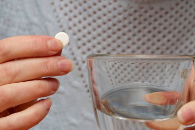 Bir kişi tableti bir bardak suyun üzerinde tutarak almaya hazırlanır..