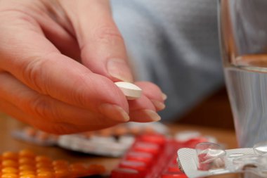 Yanında su ve çeşitli ilaçlar bulunan bir tablet tutan kişi..