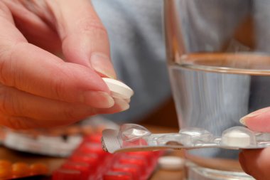 Bireyler yakınlarda bir bardak suyla beyaz bir hap almaya hazırlanıyor..