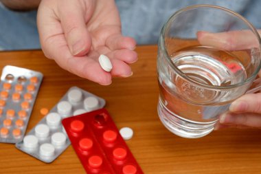 İnsan, yanında beyaz bir hap ve bir bardak su ile ilaç almaya hazırlanıyor..