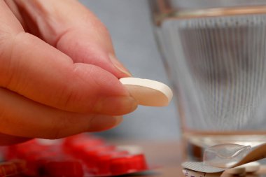 Bir el, bir bardak suyla birlikte almaya hazırlanırken bir hapı tutar..