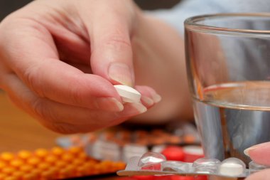 Bir el, bir bardak suyun üzerinde beyaz bir tablet tutar, tüketime hazırdır..