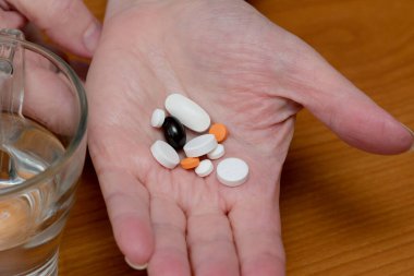 Bir bardak temiz suyun yanında çeşitli haplar sergiliyor..