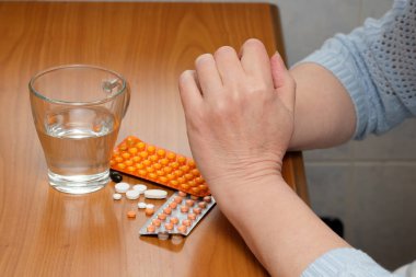 Bir insan sessizce oturur, ellerini sıkar, elinde haplar ve suyla..