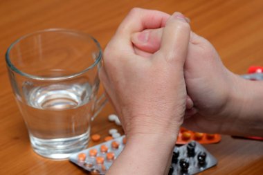 Eller birbirine sıkıca tutunur, masada bir bardak su ve çeşitli haplara bakar..