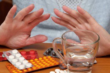 Eller çeşitli ilaç paketlerinin üzerine yerleştirildi ve bir bardak su kullanıma hazır..