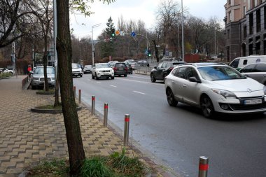 Arabalar gri gökyüzünün altında ağaçlarla ve binalarla dolu hareketli bir caddede yol alıyorlar. 24 Kasım 2025 Kyiv, Ukrayna