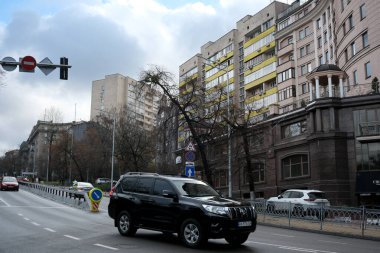 Uzun binalar ve ağaçlarla çevrili işlek bir cadde boyunca siyah bir araç sürüyor. 24 Kasım 2025 Kyiv, Ukrayna