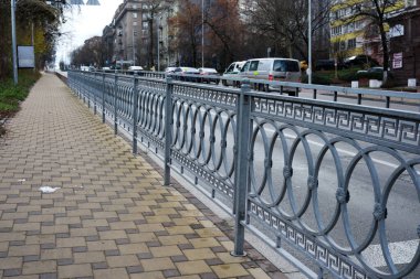 Dekoratif metal bir çit işlek bir caddenin yanındaki sessiz bir kaldırımla sınırlıdır. 24 Kasım 2025 Kyiv, Ukrayna