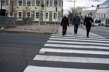 Üç kişi bulutlu gökyüzünün altındaki yaya geçidinde sakince yürüyor. 24 Kasım 2025, Kyiv, Ukrayna, Shevchenko Bulvarı