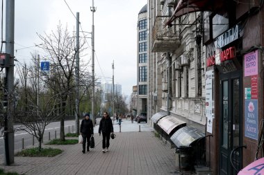 Gri gökyüzünün altında tomurcuklanan ağaçlarla dolu kalabalık bir caddede yürüyen iki kişi. 24 Kasım 2025, Kyiv, Ukrayna, Shevchenko Bulvarı