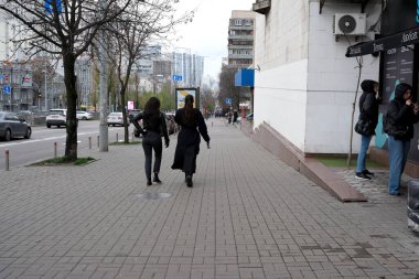 Ağaçlar çiçek açmaya başlarken iki kadın şehir kaldırımında yürüyor. 24 Kasım 2025, Kyiv, Ukrayna, Shevchenko Bulvarı