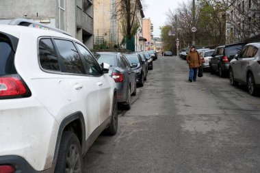 Park halindeki araçlarla dolu huzurlu bir caddede yürüyen bir adam. 24 Kasım 2025, Kyiv, Ukrayna, Shevchenko Bulvarı