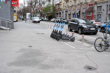 Bir sıra elektrikli scooter park halindeki arabaların yakınındaki işlek bir şehir yolunda sürücüleri bekliyor. 24 Kasım 2025 Kyiv, Ukrayna, Galitska Meydanı.