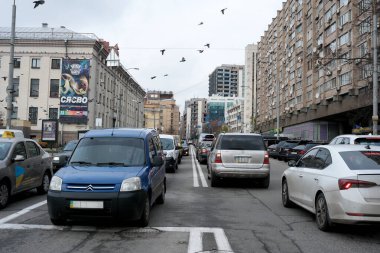 Kuşlar gri gökyüzünde zarif bir şekilde uçarken arabalar işlek caddede kuyruk oluşturur. 24 Kasım 2025 Kyiv, Ukrayna, Galitska Meydanı.