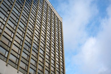 Yansıtıcı pencereli uzun yapı, parlak bir gökyüzüne karşı duruyor, huzuru çağrıştırıyor..