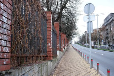 Soğuk bir şehir ortamında, tuğla bir çitin yanında sessiz bir kaldırım var..