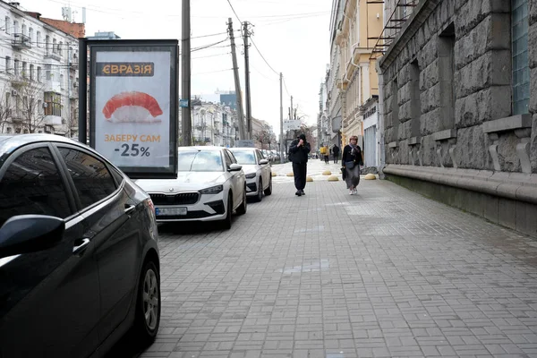 Park halindeki arabalarla dolu temiz bir kaldırımda yürüyen iki kişi. 24 Kasım 2025 Kyiv, Ukrayna