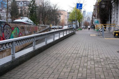 İnsanlar gri bir gökyüzünün altında renkli graffitilerle süslenmiş geniş bir kaldırım boyunca yürürler. Kyiv, Ukrayna, 26 Kasım 2025.
