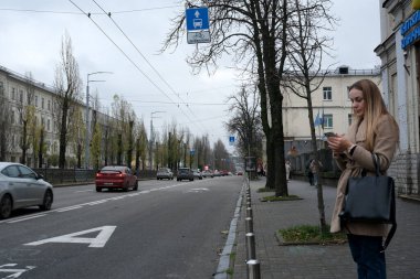 Bir kadın kaldırımda duruyor, arabaları geçerken telefonuyla meşgul oluyor. Kyiv, Ukrayna, 26 Kasım 2025.