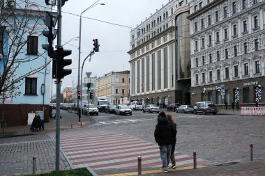 Arabalar uzaktaki bir trafik lambasında beklerken iki kişi cadde boyunca yürür. Kyiv, Ukrayna, 26 Kasım 2025.