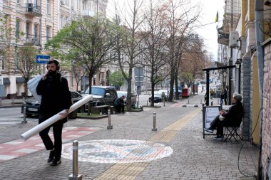 Başkaları sokaklarda çeşitli faaliyetlerde bulunurken bir adam rulo kağıt taşır. Kyiv, Ukrayna. 26 Kasım 2025.