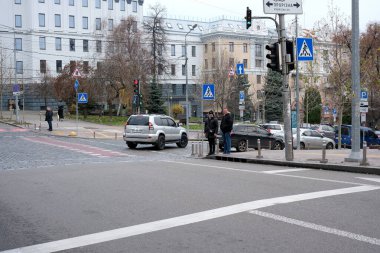 Arabalar hareketli bir caddeden geçerken iki kişi yaya geçidinde bekliyor. Kyiv, Ukrayna. 26 Kasım 2025.