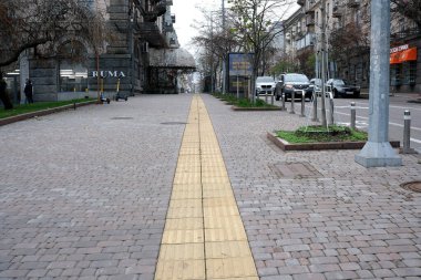 Ağaçlar ve binalarla dolu boş bir şehir caddesi çarpıcı sarı bir yol gösteriyor. Kyiv, Ukrayna. 26 Kasım 2025.