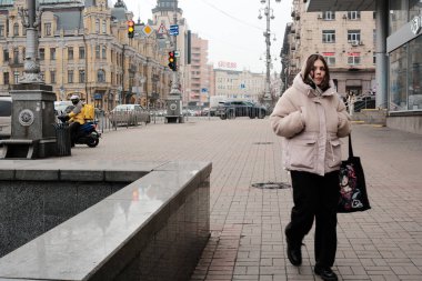 Genç bir kadın rahat bir ceketle canlı bir şehir meydanında güvenle yürüyor. Kyiv, Ukrayna. 16 Aralık 2025.