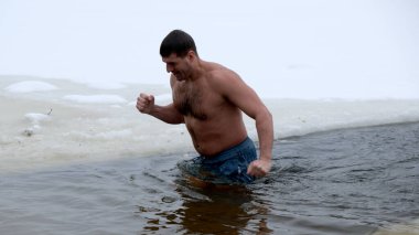 Kararlı bir adam kendini karla çevrili serin sulara daldırır. Kyiv, Ukrayna, 6 Ocak 2026. Epifani 'de buz deliği banyosu.
