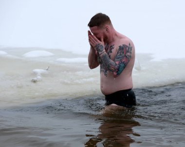 Cesur bir anda, bir adam soğuk sulara dalıp kışın güzelliğini kucaklıyor. Kyiv, Ukrayna, 6 Ocak 2026. Epifani 'de buz deliği banyosu.