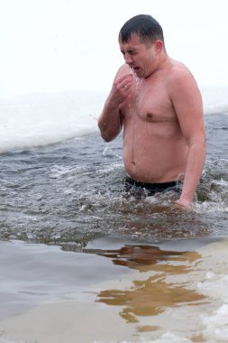 Bir adam kışın buzlu suya göğüs gerer, heyecan verici bir an yaşar. Kyiv, Ukrayna, 6 Ocak 2026. Epifani 'de buz deliği banyosu.