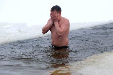 Bir adam buz gibi suda durur, yüzünü kapatırken soğukla yüzleşir, cesaret gösterir. Kyiv, Ukrayna, 6 Ocak 2026. Epifani 'de buz deliği banyosu.