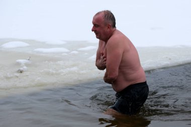 Yüzen buzlarla çevrili soğuk suda yüzen bir adam kışın soğuğunu kucaklıyor. Kyiv, Ukrayna, 6 Ocak 2026. Epifani 'de buz deliği banyosu.