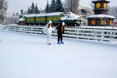 İki arkadaş, karlı bir manzarayla çevrili bir buz pistinde neşeyle kayıyorlar. Kyiv, Ukrayna, Ukrayna Expocenter 'ı. 14 Ocak 2026.