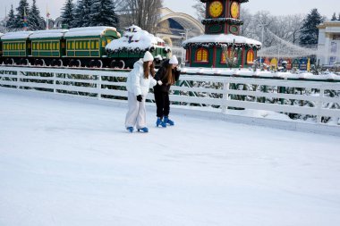İki arkadaş tatil ruhuyla dolu karlı bir buz pistinde süzülüyor. Kyiv, Ukrayna, Ukrayna Expocenter 'ı. 14 Ocak 2026.