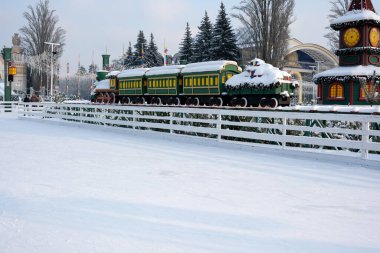 Renkli bir tren kış parkı manzarasına neşe katarak karla süslenir. Kyiv, Ukrayna, Ukrayna Expocenter 'ı. 14 Ocak 2026.